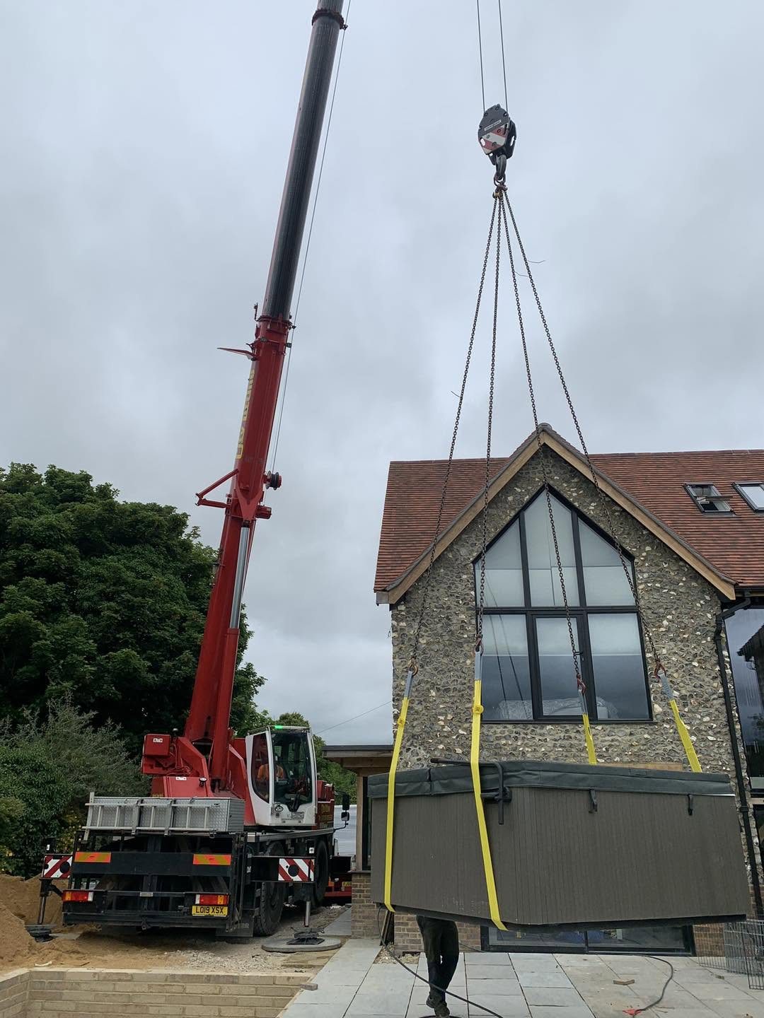 A crane lifting a swim spa into a back garden